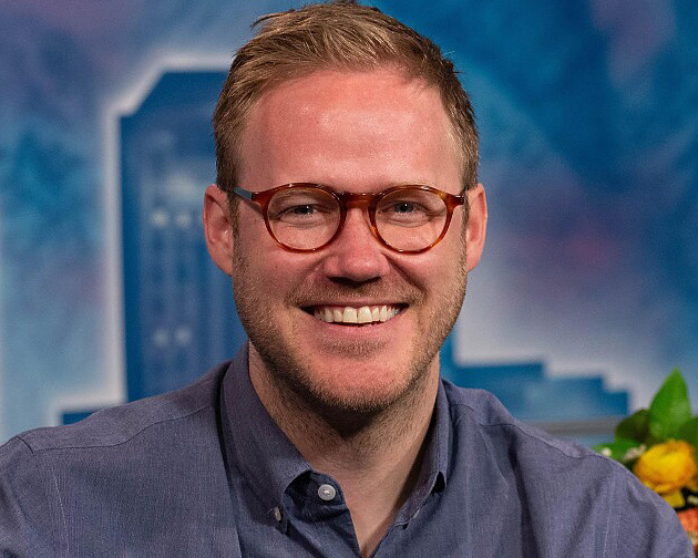 Headshot of John smiling at the camera with a blue background