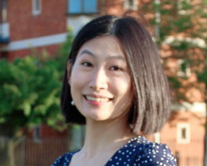 Edith with smiling at the camera with the left side of her hair tucked behind her ear. 